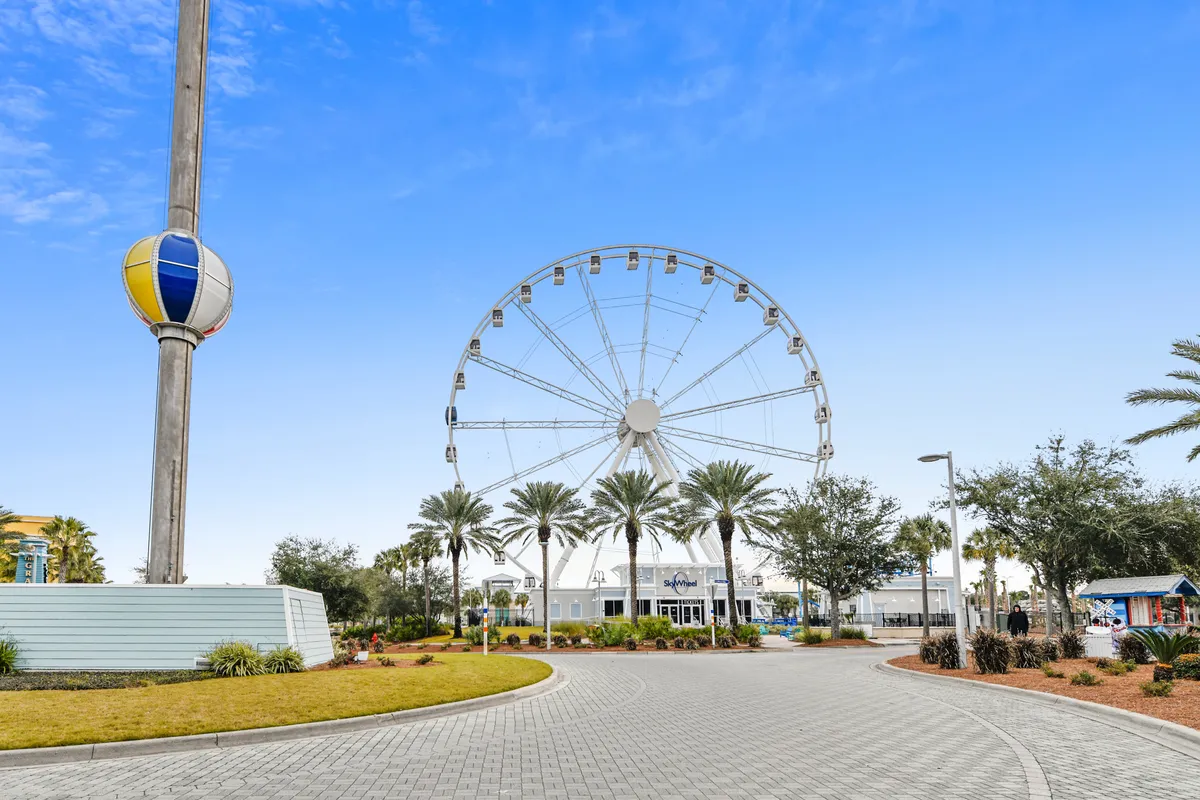 A festive exterior shot of a ferris wheel surrounded by palm trees, with the entrance area inviting visitors to enjoy rides and seasonal events. The scene conveys excitement and the potential for shared memories at local attractions.