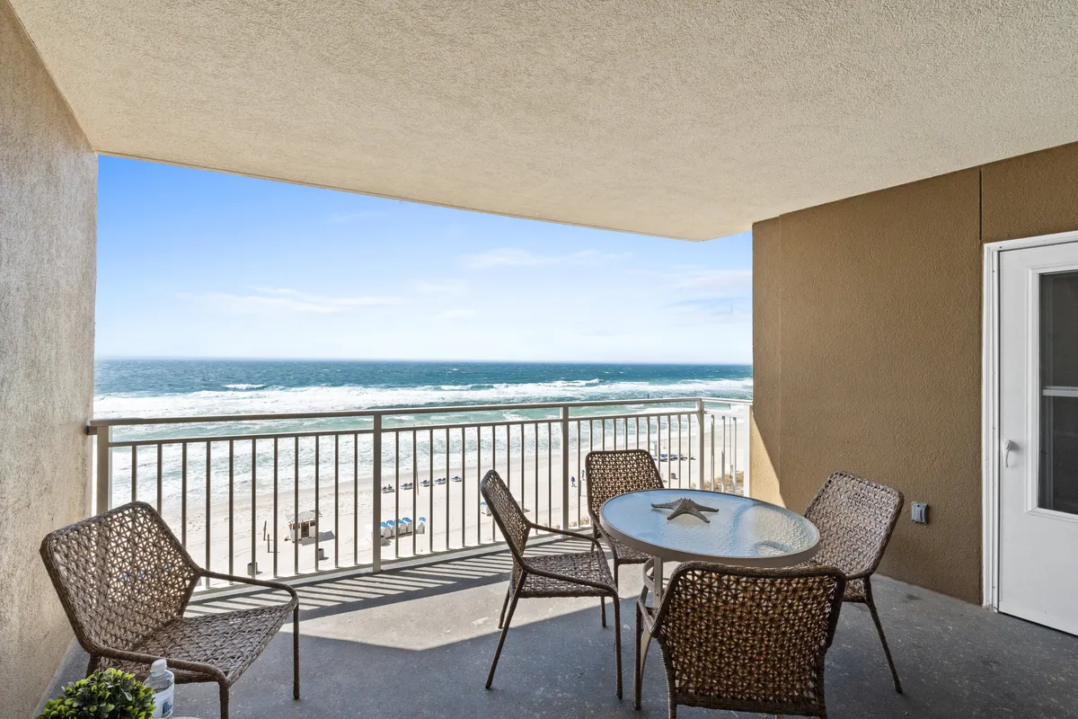 This image features an inviting balcony outfitted with patio furniture, overlooking the ocean. The tranquil scene is perfect for enjoying a drink while watching the sunset, with railings providing an unobstructed view of the surf and sky.