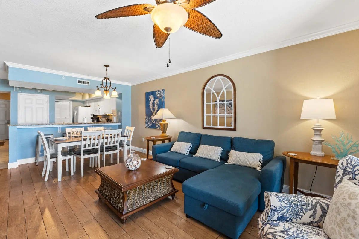 The image features a spacious living area with a comfortable sofa, a dining table, a chandelier, and tasteful artwork on the wall. The setting is casual and inviting, ideal for family gatherings and relaxation after a day at the beach. The open layout showcases the seamless flow between living and dining zones, emphasizing togetherness and entertaining possibilities.