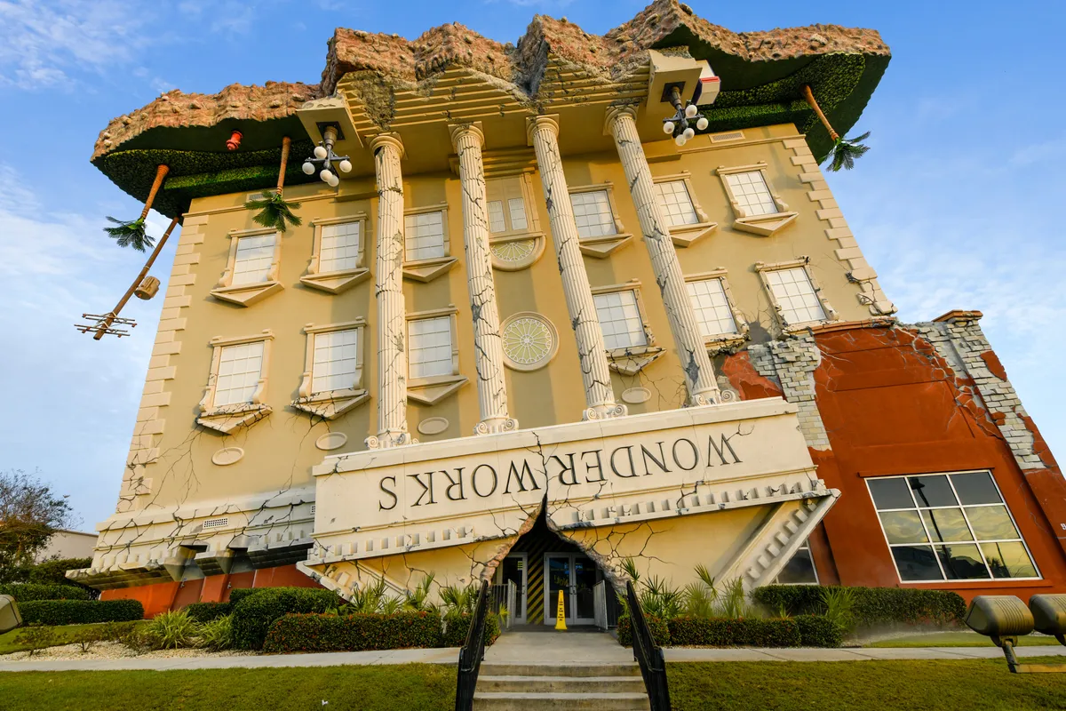 This image shows the iconic upside-down structure of WonderWorks, instantly recognizable with tropical landscaping and whimsical architectural details. Visitors are seen snapping photos, drawn to the surreal appearance and sense of fun the attraction offers.