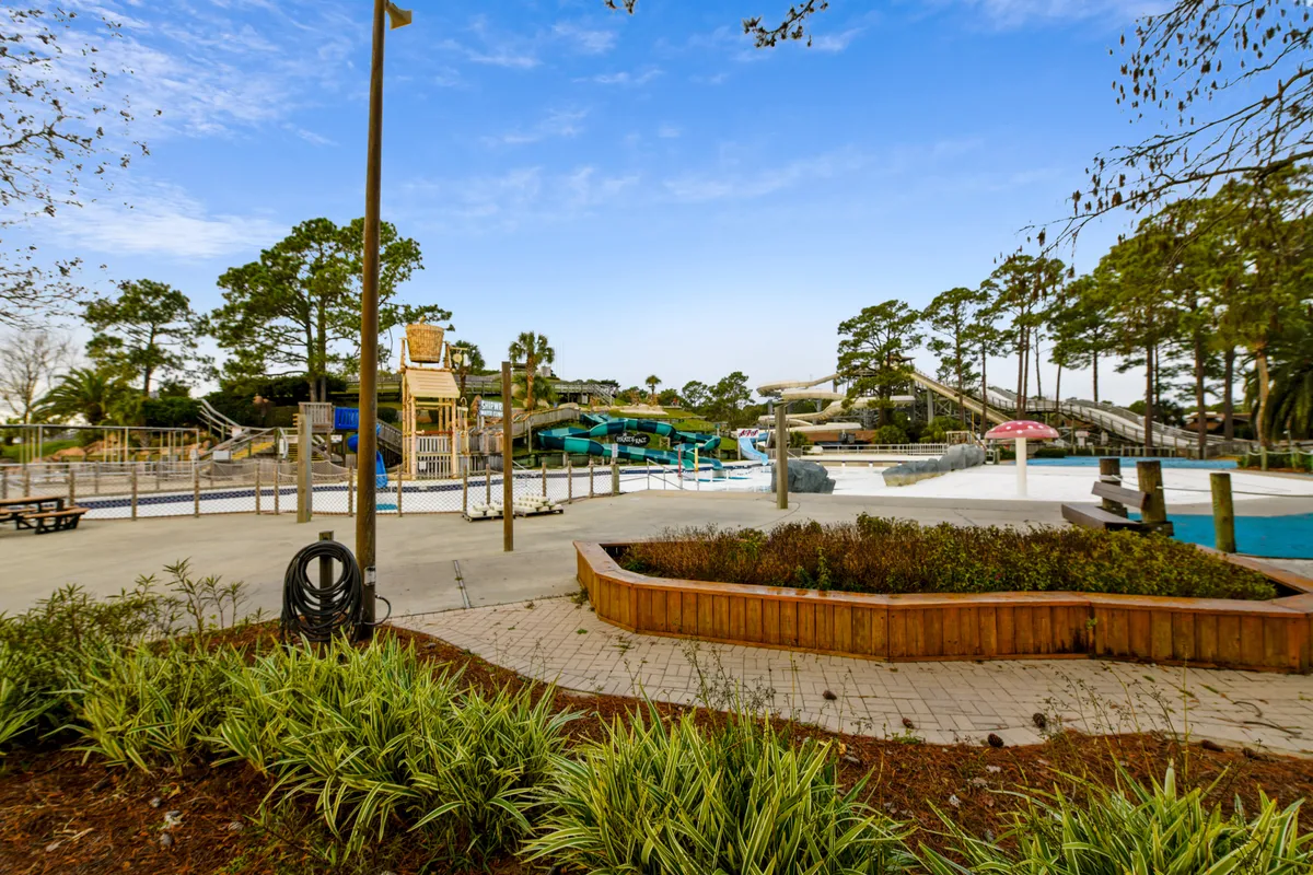 A lively outdoor water park area featuring water slides, a swimming pool, and playground equipment. The landscaped gardens and bright colors create an energetic, family-friendly vibe—ideal for seasonal fun and complimentary local attraction experiences.