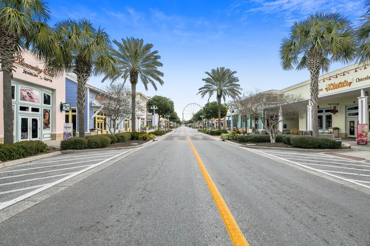 This lively scene captures the storefronts, palm trees, and the distant ferris wheel at Pier Park, showcasing a vibrant street perfect for shopping, dining, and enjoying live entertainment.