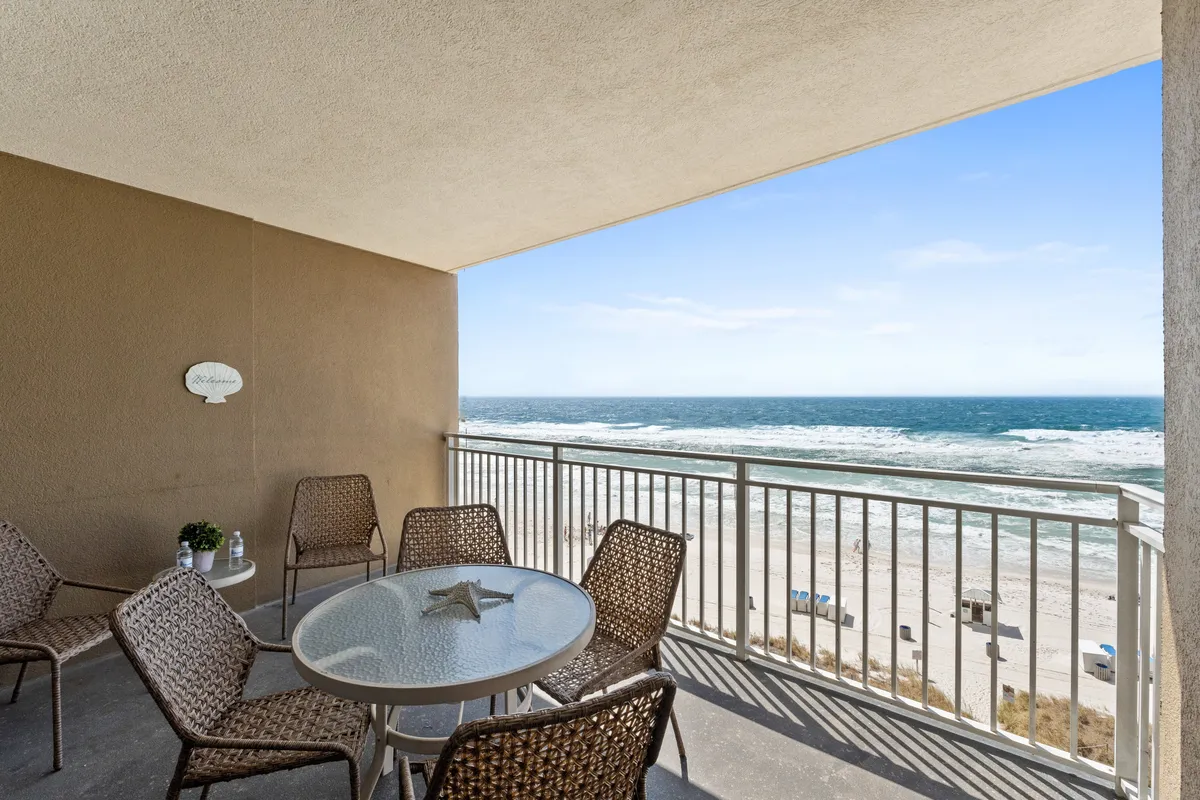 The image captures a serene private balcony with comfortable seating, a table adorned with a starfish centerpiece, and sweeping ocean views. The setting is perfect for enjoying morning coffee, hosting small gatherings, or watching spectacular Gulf Coast sunsets.
