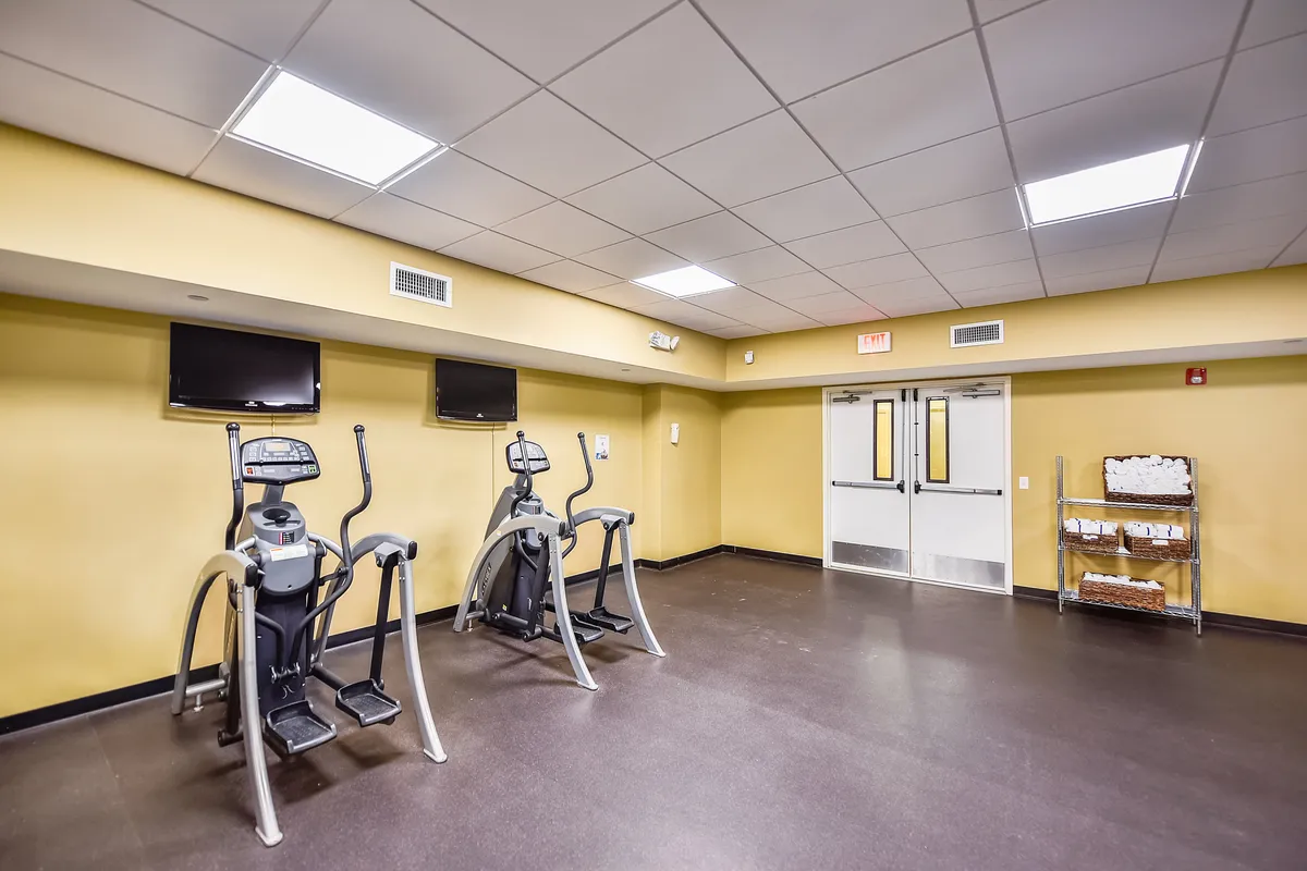 A bright, modern fitness center with elliptical machines, televisions mounted above, and an exit door providing natural light. The space looks clean, energetic, and perfectly suited for guests who want to maintain their workout routines while on vacation.