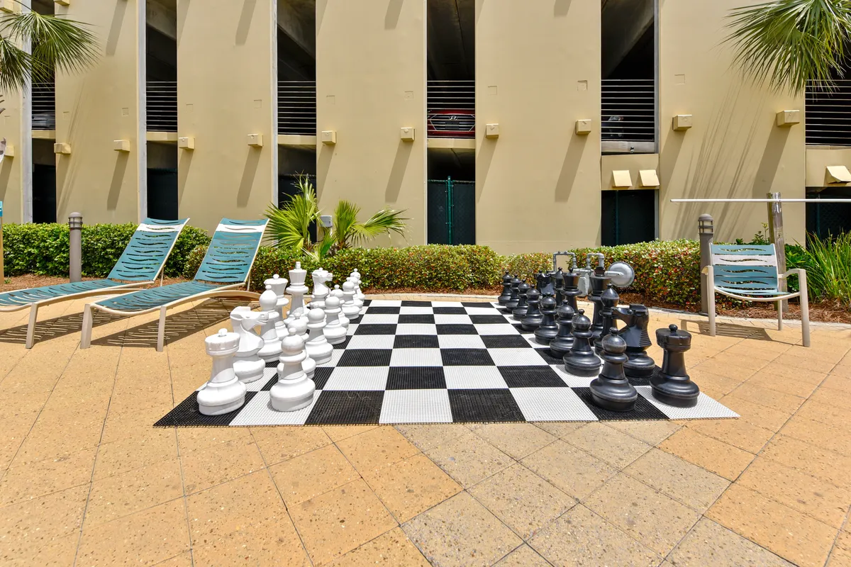An outdoor communal area featuring a large chess set, lounge chairs, and well-maintained landscaping. The scene is playful, with ample space for groups to relax or interact, suggesting fun activities outside of the beach and pool.