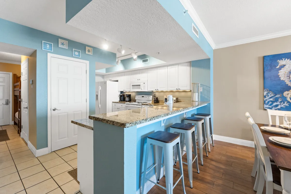 An inviting interior shot with a granite-topped kitchen island, bar stools, and a dining table set for meals. Artistic wall décor adds warmth, and the open layout encourages socializing and group gatherings.