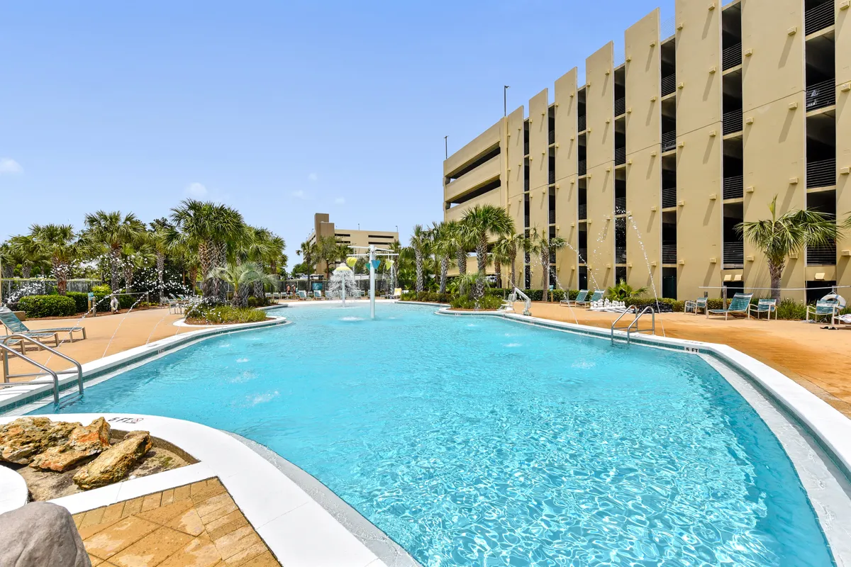 A sparkling swimming pool bordered by palm trees and lounge chairs, with a water fountain adding to the resort ambiance. The pool area feels lively and inviting, perfect for leisurely swims and sunbathing, with a hint of luxury and relaxation.